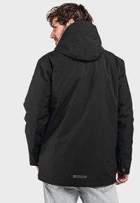 Schwarze wasserdichte Jacke mit Kapuze, die eine glatte Textur und eine leicht verlängerte Form aufweist. Enthält ein Etikett am hinteren Saum.