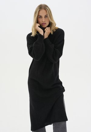 Schwarzes, gestricktes Kleid mit Rollkragen, langen Ärmeln und lockerer Passform, das eine strukturierte Oberfläche und einen asymmetrischen Saum aufweist.