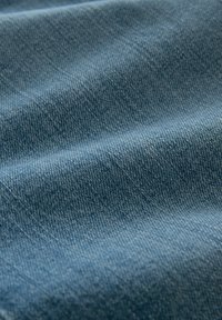 Denim tkanina u srednje plavoj nijansi s vidljivom teksturom tkanja, koja prikazuje nabore i pregibe za prirodno pada.