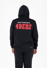 Zwarte hoodie met capuchon, met rode tekst: "SAN FRANCISCO 49ERS" op de achterkant. Machinaal gebreide stof met ribgebreide manchetten en zoom.