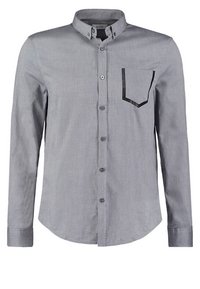 Camiseta de manga larga gris hecha de un tejido con textura suave. Cuenta con un cuello abotonado y un bolsillo con un contorno negro contrastante.