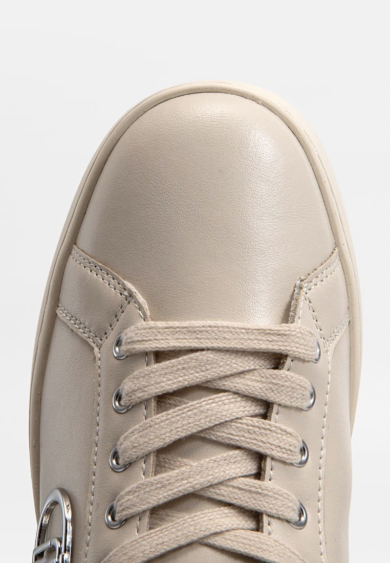 Zapatillas de cuero beiges con punta redonda, cordones del mismo tono, ojales de metal y un detalle acentuado en el lateral. Textura suave y diseño minimalista.