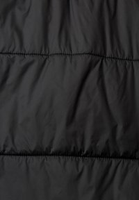 Giacca a vento nera in un materiale morbido, con sezioni trapuntate orizzontali e cuciture visibili.