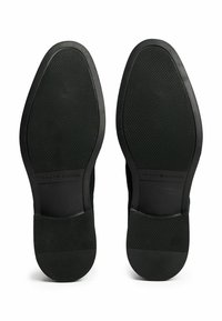 Sole nere in gomma di scarpe eleganti con pattern di grip testurizzato e branding "Tommy Hilfiger" vicino all'area dell'arco.