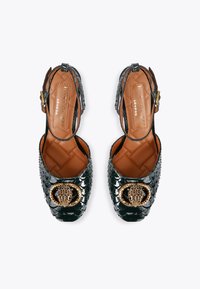 Des chaussures en cuir verni noir avec texture crocodile, embellissement en métal doré, boucle ajustable et semelle intérieure matelassée marron.