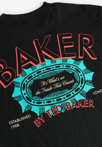 Camiseta de algodón negra con letras rojas en negrita "BAKER" y un gráfico turquesa con diseño circular. El texto incluye "By Ted Baker" y "Establecido en 1988".
