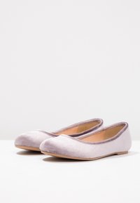 Ett par ljuslila sammet ballerina-skor med rundade tår och beige innersulor på en vit yta.