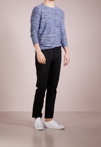 Blue marled long-sleeve sweater worn with black slim-fit pants and white sneakers, standing on a neutral floor with a light background.