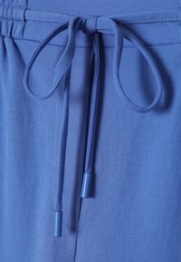 Modré látkové šortky s elastickým pasem a šňůrkou na stažení. Konce šňůrky jsou také modré. Materiál působí hladce a lehce.