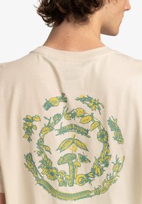 Cream-colored cotton t-shirt with a large green and yellow botanical and mushroom print on the back, featuring intricate detail and texture.