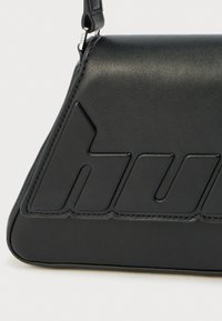 Μαύρη δερμάτινη τσάντα με δομημένο σχέδιο, με ανάγλυφο λογότυπο και λεπτομερείς ραφές. Περιλαμβάνει αποσπώμενο ιμάντα ώμου.