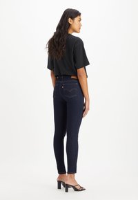 Smala jeans i mörkblå denim med hög midja, med en brun läderlapp och kontrasterande gula sömmar; kombinerat med en svart t-shirt.