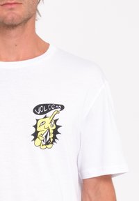 Witte katoenen T-shirt met een gele cartoonfiguur graphic met zwarte accenten en tekst "VOLCOM" boven het ontwerp op de borst.
