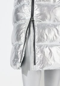 Silberne Pufferjacke mit glänzender, metallischer Oberfläche. Besitzt einen doppelten Reißverschluss an der Front und ein gestepptes Design mit gepolsterten Abschnitten.