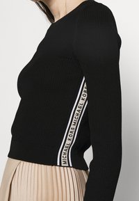 Maglione nero a coste con maniche lunghe, scollo a girocollo e striscia laterale a contrasto con il testo "MICHAEL KORS".