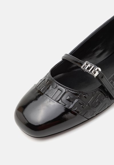 Pantofle din piele patent neagră, cu vârf rotund, având o bandă texturată și o cataramă argintie. Designul include un model de logo proeminent.