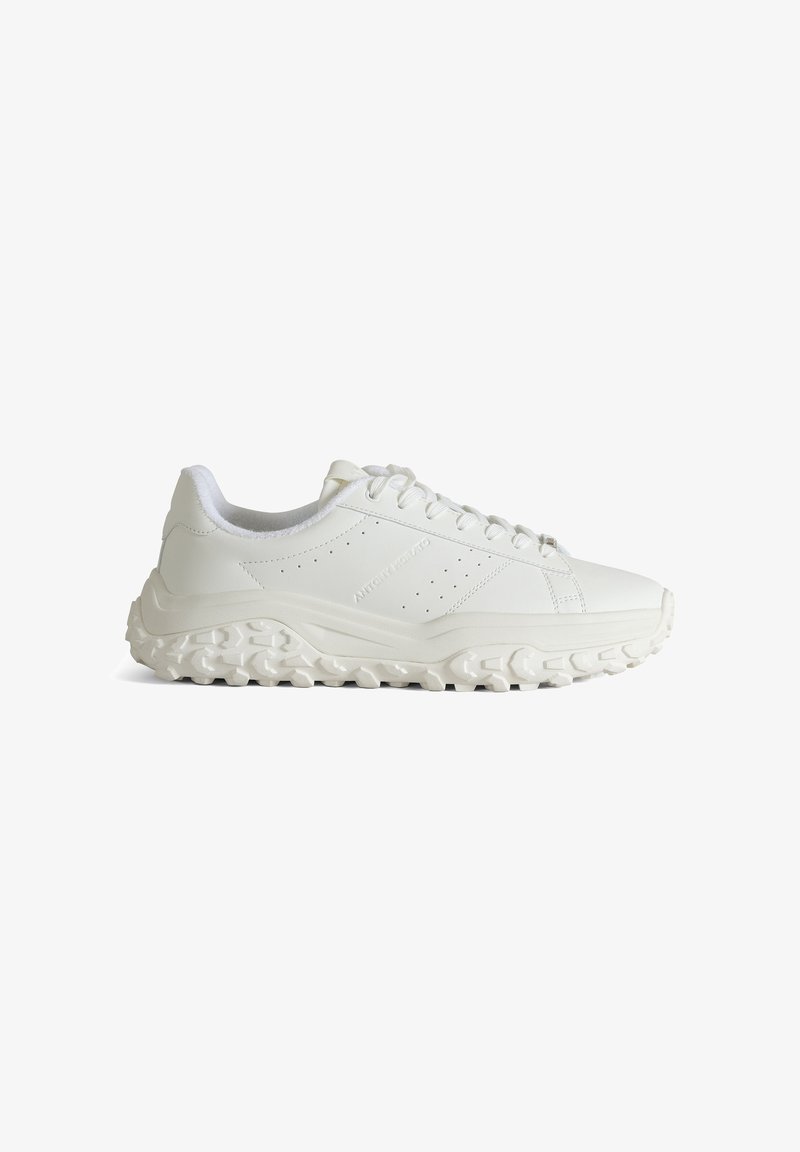 Baskets blanches basses avec semelle épaisse texturée, fermeture à lacets à l'avant et détails latéraux perforés subtils.