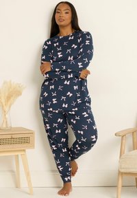 Granatowy komplet piżamowy z długimi rękawami i spodniami, zdobiony różowymi motywami w kokardki. Wykonany z miękkiego materiału, ma luźny krój.