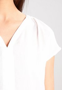 Weiße kurzärmlige Bluse mit V-Ausschnitt und weichem, leichtem Stoff. Verfügt über subtile Drapierungen an den Schultern und eine lockere Passform.