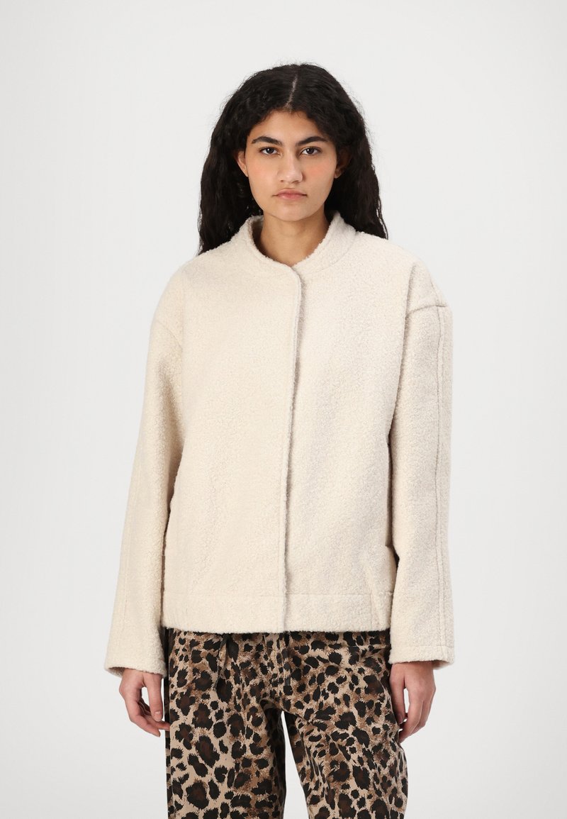 Cremfarbener Fleece-Jacke mit rundem Kragen, fallenden Schultern und lässiger Passform, kombiniert mit gemusterten Leopardenprint-Hosen.