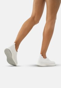 Baskets blanches à enfiler avec une tige en tricot texturé et une semelle légère. Elles comprennent des accents élastiques pour un enfilage facile et un design à bout rond.