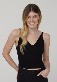 Crop top nero a coste con scollo a V e spalline sottili, realizzato in un tessuto testurizzato. Il modello indossa jeans neri a vita alta.