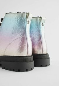 Bottines iridescentes avec une texture plissée, semelle en caoutchouc noir et accents d'étoile argentés sur le talon, dotées d'un laçage.