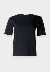 Camiseta negra de manga corta en un material suave, con un gran volante texturizado en el hombro izquierdo y un sutil bordado decorativo.