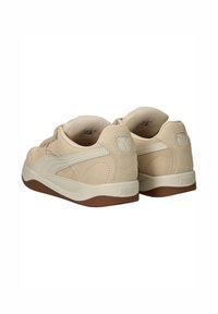 Een paar beige Puma sneakers met suède accenten, crèmekleurige zijstrepen, gevoerde kraag en bruine rubberen zolen, zichtbaar vanuit een achteraanzicht.