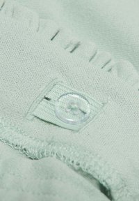 Vaalean mintunvihreä kangas, jossa on teksturoidun pinnan lisäksi selkeä nappi ja ommeltu reuna, korostaen pientä laskostesarjaa.