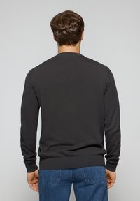 Ciemnoszara bluza z okrągłym dekoltem, wykonana z miękkiego materiału, z długimi rękawami i ściągaczami przy mankietach, noszona z niebieskimi jeansami.