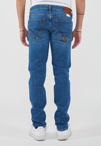 Jeans in denim blu con una vestibilità aderente, caratterizzati da una patch in pelle con logo, design delle tasche posteriori cucito e una texture leggermente sbiadita.