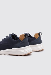 Zapatillas de navy con parte superior de tejido texturizado, acentos de cuero marrón y suela de goma blanca; cuentan con una lengüeta y detalles reflectantes.