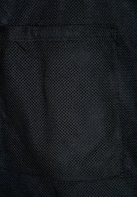 Tissu en maille noire avec un motif en losange, doté d'une poche cousue. La texture est légèrement rugueuse et respirante, ce qui améliore la durabilité.