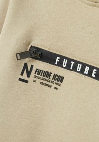 Felpa beige con tasca con zip, caratterizzata da un'etichetta nera con la scritta "FUTURE ICON" e dettagli di design con logo.