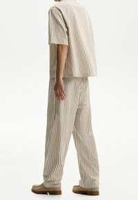 Randig tvådelad outfit i beige och brunt, bestående av en lös kortärmad skjorta och vida byxor med en mjuk textur.