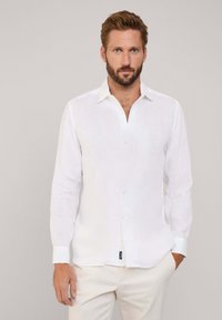 Chemise blanche en lin à manches longues avec un col classique et une fermeture à boutons. Présente une texture subtile et une petite étiquette de marque à l'ourlet.