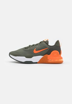 Baskets basses de sport vert foncé avec des accents orange vif, une semelle intermédiaire blanche et un amorti à air visible au talon.