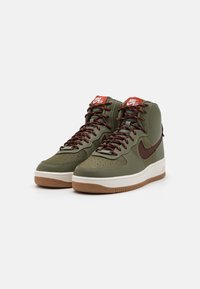 High-top sneakers in olive green leather with brown accents. Features padded collar, perforated toe, and contrasted laces. Gum rubber sole.
