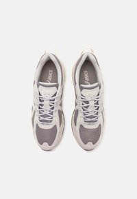 Scarpe atletiche grigie con upper in mesh, accenti bianchi e suole in gomma testurizzata. Design con lacci e logo sulla linguetta e sui lati.