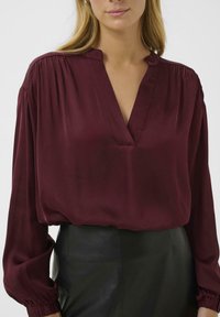 Burgundy silk blouse with a V-neck, pleated shoulders, and long, gathered sleeves, paired with a black leather skirt.