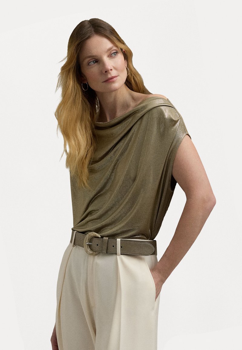 Metallisch goldfarbene Bluse mit kurzen Ärmeln, kombiniert mit cremefarbenen Hosen und einem passenden metallischen Gürtel mit einer runden Schnalle.