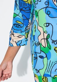 Haut à manches courtes multicolore avec des motifs abstraits en bleu, vert et jaune. Fabriqué en tissu lisse et léger avec une coupe décontractée.