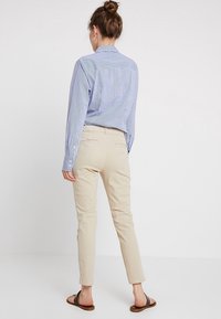 Modro-bílá pruhovaná košile s límečkem, spárovaná se světle béžovými kalhotami. Kalhoty mají dvě zadní kapsy a slim fit design.