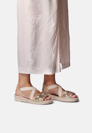 Stopy noszące beżowe koturny z kwiatowym wzorem i paskami w kształcie krzyża oraz biała spódnica do kostek z bocznym rozcięciem.