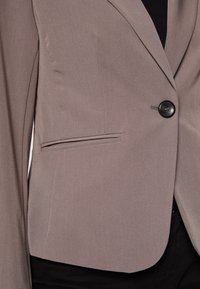 Grå kavaj i en slät tygkvalitet, med en ensam svart knapp, snittad krage och en sidoficka med en elegant design.