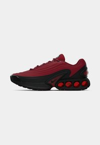 Red and black athletic shoe with a textured upper, smooth leather accents, prominent curved sole, and distinct circular air cushioning elements.