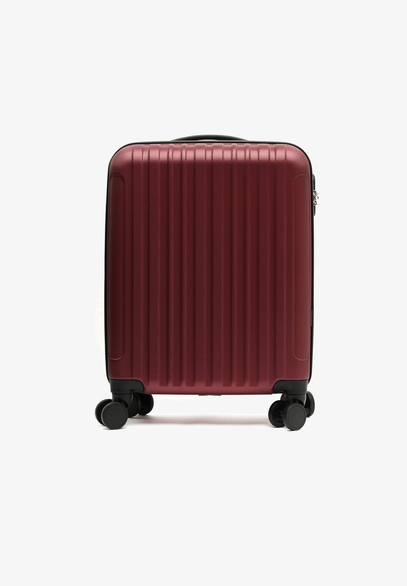 Hard-shell kastanjebruine koffer met verticale ribbels, vier zwarte zwenkwielen en een bovenhandvat tegen een witte achtergrond.