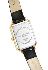 Montre rectangulaire avec un fond en acier inoxydable, un boîtier doré, un bracelet en cuir noir et des détails gravés au dos.