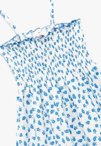 Vestido blanco sin mangas con patrón floral azul y corsé fruncido, que presenta tirantes finos y un borde de escote con volantes.